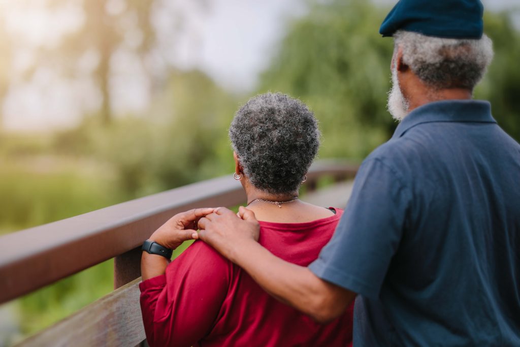 An older couple stands on a bridge holding hands.