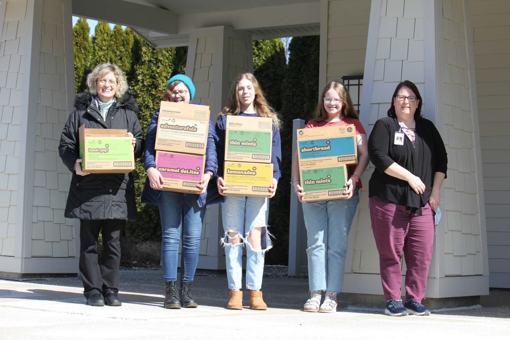 girls and women holding boxes of girl scout cookies they are donating