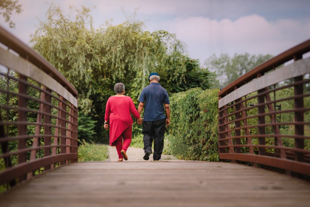 An older couple walks across a bridge holding hands