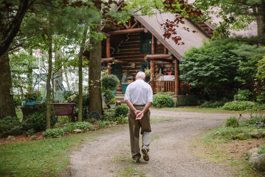 Older man walking on a path in front of a log cabin