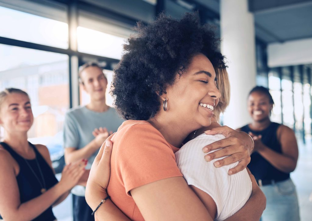 African American woman hugging another person with people clapping behind them